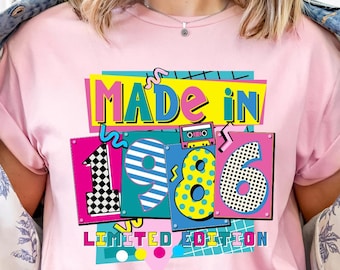 May include: A pink t-shirt with the text "MADE IN 1986 LIMITED EDITION" in a colourful graphic. The design includes a cassette tape, chequered squares, and polka dots. The shirt is worn with a denim jacket.