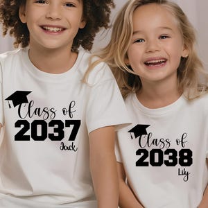 May include: Two children wearing off-white t-shirts with black text. The shirts say "Class of 2037 Jack" and "Class of 2038 Lily" with a graduation cap graphic. The children are smiling.