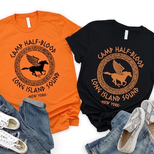 May include: Two t-shirts, one orange and one black, with a circular graphic featuring a winged horse and the text "CAMP HALF-BLOOD LONG ISLAND SOUND - NEW YORK." The shirts are paired with jeans, sunglasses, and shoes.