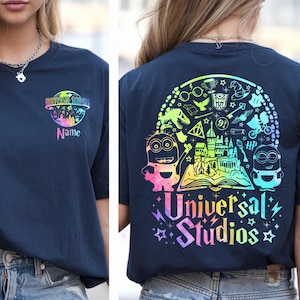 May include: Navy blue t-shirt with a colorful Universal Studios graphic on the front and back. The front features a logo and the word "Name". The back has a rainbow design with cartoon characters and the words "Universal Studios".