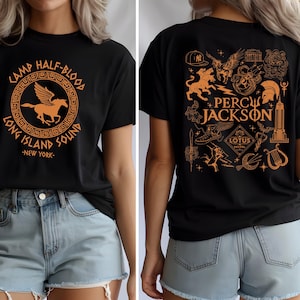 May include: Black t-shirt featuring a circular design with a winged horse and the text "CAMP HALF-BLOOD LONG ISLAND SOUND NEW YORK" in orange. The back of the shirt has various orange illustrations and the words "PERCY JACKSON".