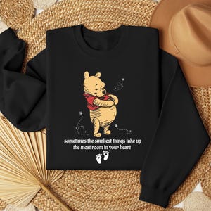 May include: Black sweatshirt with a Winnie the Pooh illustration and the text "sometimes the smallest things take up the most room in your heart".