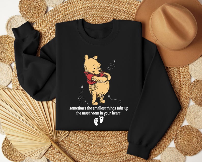 May include: Black sweatshirt with a Winnie the Pooh illustration and the text "sometimes the smallest things take up the most room in your heart".