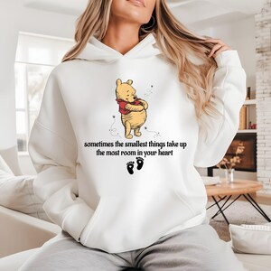 May include: White hoodie with a Winnie the Pooh illustration and the text "sometimes the smallest things take up the most room in your heart".