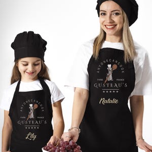 May include: Two people wearing black aprons with a cartoon rat chef design. The aprons say "Anyone Can Cook" and "Gusteau's" with the names "Natalie" and "Lily" printed below.