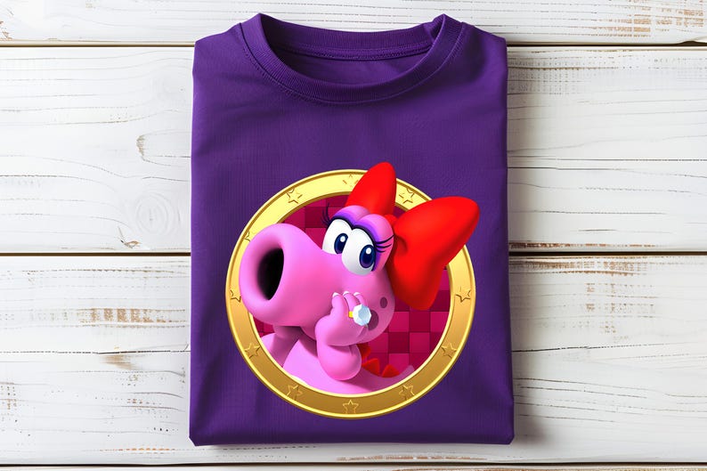 Peut inclure: Un t-shirt violet avec un personnage de dessin anim&eacute; rose, un n&oelig;ud rouge et une bague, dans un cercle dor&eacute;. Le t-shirt est pli&eacute; sur une surface en bois blanc. Le t-shirt est pli&eacute; sur une surface en bois blanc.