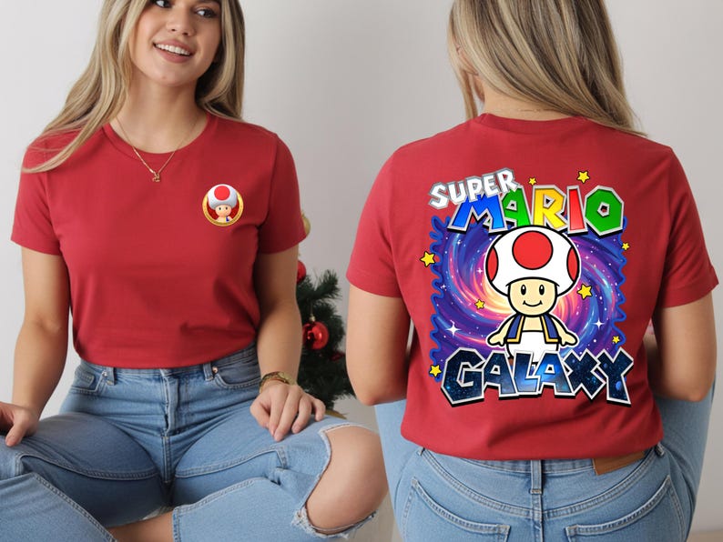 May include: Red t-shirt featuring a Super Mario Galaxy design. The front of the shirt has a small Toad graphic. The back of the shirt displays a larger graphic of Toad with the words "Super Mario Galaxy".
