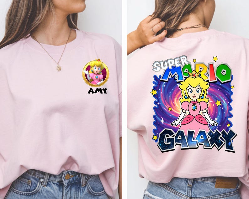 May include: A light pink t-shirt featuring a cartoon image of Princess Peach from Super Mario. The front of the shirt has a circular graphic with the princess and the name "AMY" below. The back of the shirt has the words "SUPER MARIO GALAXY" with a galaxy background.