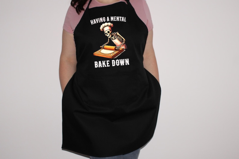May include: Black apron with a skeleton chef rolling out dough. The text on the apron reads "Having a mental bake down."