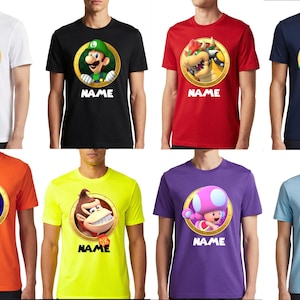 May include: A collection of eight short-sleeve t-shirts in white, black, red, navy, orange, neon yellow, purple, and light blue. Each shirt features a circular graphic of a Nintendo character and the word NAME printed in black below the circle.