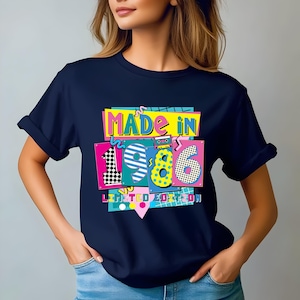 K&ouml;nnte beinhalten: Marineblaues T-Shirt mit einem farbenfrohen Aufdruck "MADE IN 1986 LIMITED EDITION". Das Design zeigt die Zahlen 1, 9, 8 und 6 in verschiedenen Mustern und Farben, sowie eine Kassettenband-Grafik.