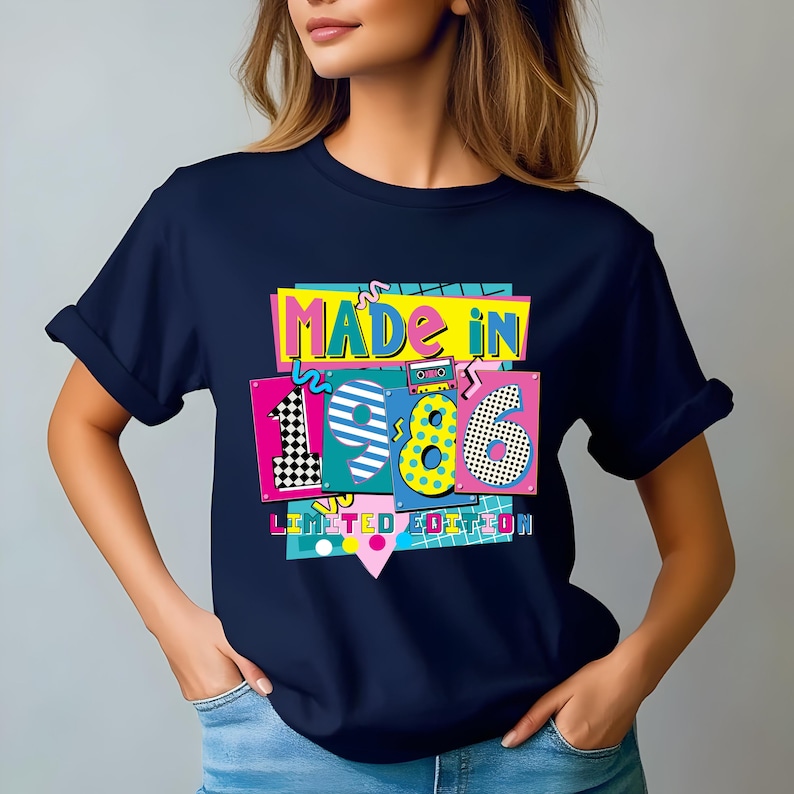 K&ouml;nnte beinhalten: Marineblaues T-Shirt mit einem farbenfrohen Aufdruck "MADE IN 1986 LIMITED EDITION". Das Design zeigt die Zahlen 1, 9, 8 und 6 in verschiedenen Mustern und Farben, sowie eine Kassettenband-Grafik.
