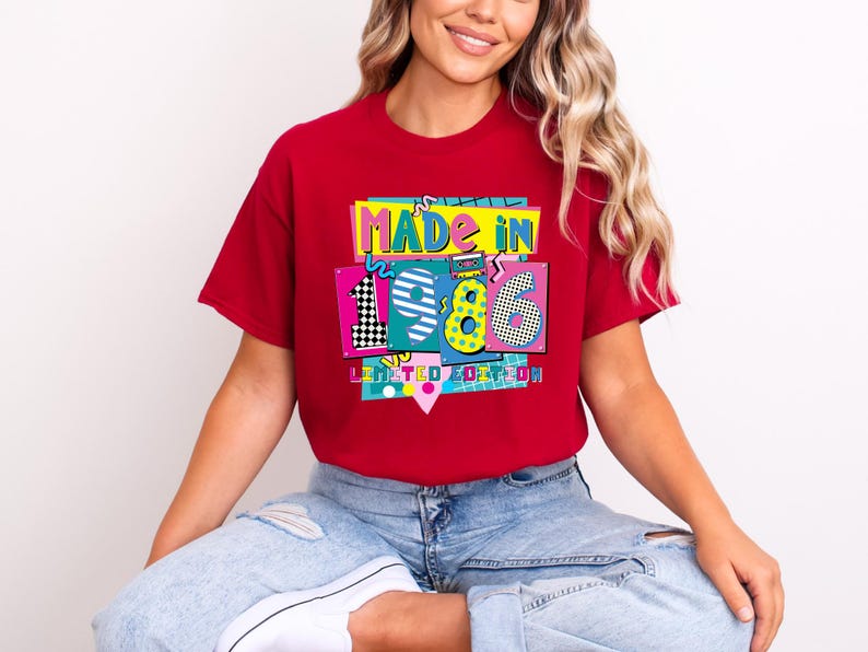 K&ouml;nnte beinhalten: Ein rotes T-Shirt mit einem farbenfrohen Aufdruck mit der Aufschrift "MADE IN 1986 LIMITED EDITION". Die Grafik zeigt die Zahlen 1, 9 und 6 in einem Retro-Stil, mit einer Kassette und einem Schachbrettmuster. Das T-Shirt wird getragen.