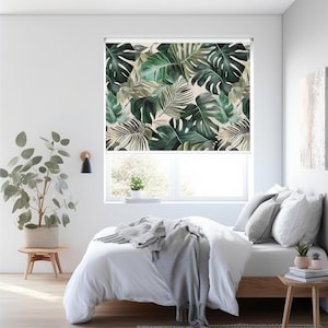 Könnte beinhalten: Ein weißes Bett mit einer grauen Tagesdecke und einem Fenster mit einem Rollladen mit tropischem Blattmotiv. Der Raum ist mit einer Topfpflanze und einem Beistelltisch dekoriert.
