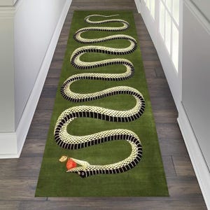 Puede incluir: Una alfombra verde con un dise&ntilde;o de serpiente en blanco y negro. La serpiente se retuerce a trav&eacute;s de la alfombra y tiene una manzana roja en la boca.