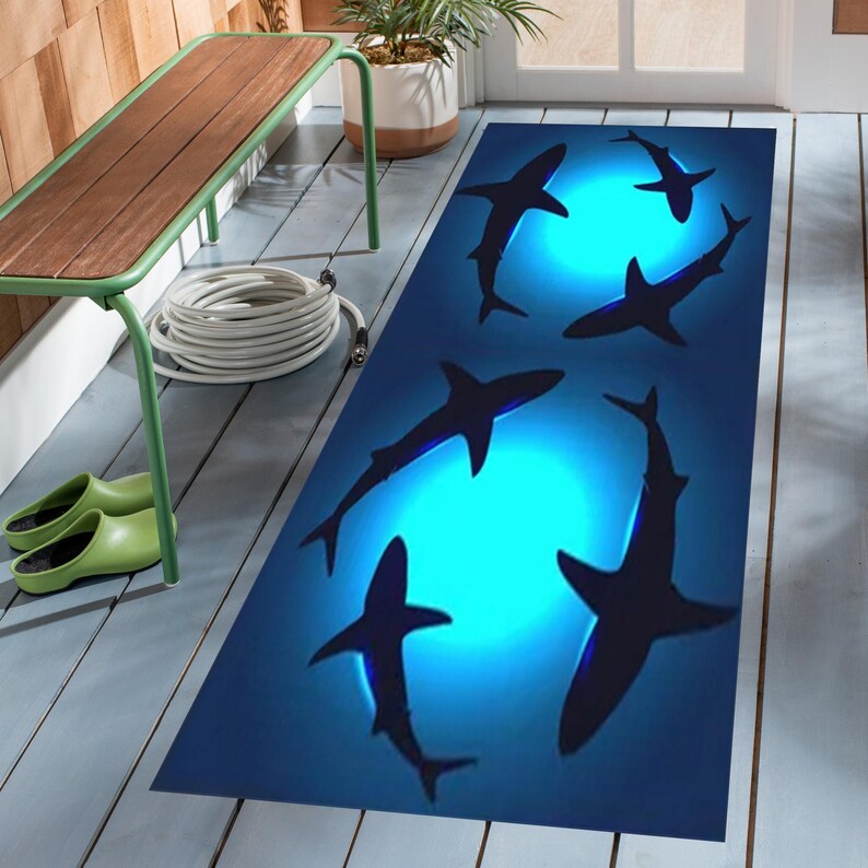 May include: A blue and black doormat with a design of five sharks swimming in a circle around a glowing blue light.
