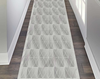 May include: A rectangular, light grey hallway runner rug featuring a geometric pattern of squares and triangles. The rug is placed on a dark wood floor, with white trim and a doorway visible in the background.
