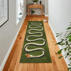 Puede incluir: Una alfombra de serpiente verde y blanca con una manzana roja en su boca. La alfombra est&aacute; colocada en un suelo de madera en un pasillo.