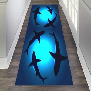 May include: A blue and black runner rug with a design of five sharks swimming in a circle around a glowing blue circle. The sharks are silhouetted against the blue background.