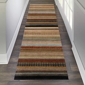 May include: A long, narrow runner rug with a striped pattern in shades of brown, beige, and red. The rug has a woven texture and a fringe border.
