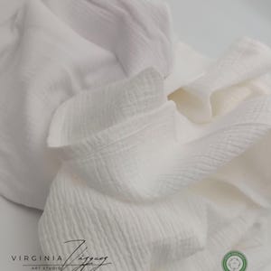 May include: White cotton fabric with a textured surface. The fabric is folded and has a label that says "Oeko-Tex Standard 100" and a QR code. The fabric also has a label that says "100% Organic Cotton".