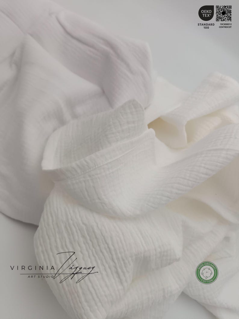 May include: White cotton fabric with a textured surface. The fabric is folded and has a label that says "Oeko-Tex Standard 100" and a QR code. The fabric also has a label that says "100% Organic Cotton".