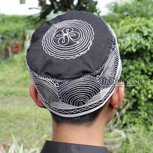 May include: Black skullcap with white embroidered circular and curved line designs. The cap has a rounded crown and a close fit. The embroidery is detailed and creates a textured appearance. The cap is worn by a person.