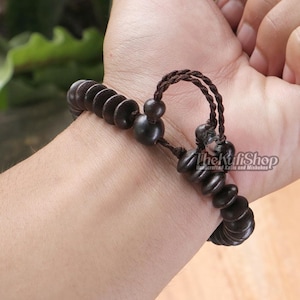 Peut inclure: Bracelet en bois brun foncé avec des perles circulaires et une fermeture en cordon tressé. Le bracelet est porté au poignet et comporte une série de perles en forme de disque brun foncé. Le cordon est de couleur brun foncé assortie.