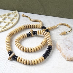May include: A wooden prayer bead necklace with alternating light and dark beads. The necklace is made of round, light-colored wooden beads interspersed with sections of black beads. The design includes a tassel and a decorative wooden piece.