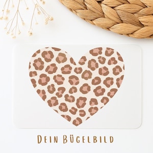 Könnte beinhalten: Eine weiße rechteckige Karte mit einem herzförmigen Leopardenmuster in Braun- und Beigetönen. Der deutsche Text "DEIN BÜGELBILD" ist unten in Braun gedruckt. Die Karte befindet sich vor einem weißen Hintergrund mit einer gewebten Textur.