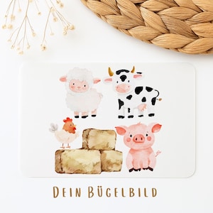 Könnte beinhalten: Eine weiße rechteckige Karte mit Aquarellillustrationen von Hoftieren: einem Schaf, einer Kuh, einem Huhn und einem Schwein. Die Tiere sind über drei Heuballen angeordnet. Der Text "DEIN BÜGELBILD" ist unten in Braun gedruckt.