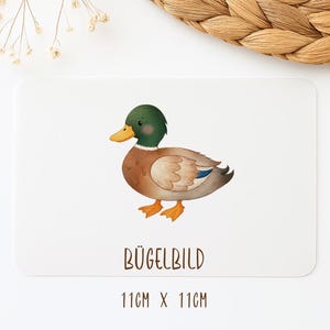 Könnte beinhalten: Eine rechteckige weiße Karte mit einer Aquarellillustration einer Stockente mit grünem Kopf, braunem Körper und orangefarbenen Füßen. Der Text BÜGELBILD ist in Braun unter der Ente gedruckt, mit den Maßen 11cm x 11cm am unteren Rand.