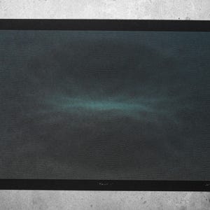 May include: An abstract art print in a black frame, featuring a dark, textured backdrop with a teal horizontal band. The artwork is displayed against a grey concrete surface, creating a stark contrast.