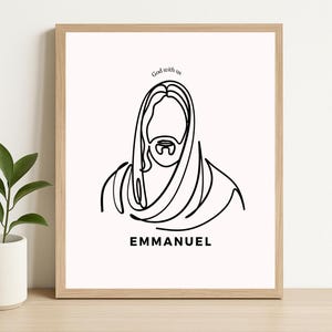 Puede incluir: Una impresión enmarcada con un dibujo lineal minimalista de una figura religiosa con barba y pelo largo. Las palabras "God with us" están encima de la imagen, y la palabra "EMMANUEL" está debajo. El marco es de color marrón claro.