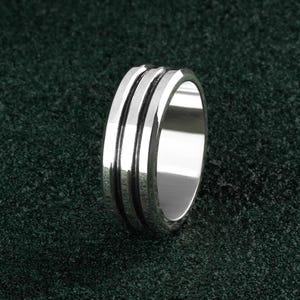 May include: A silver ring with three grooves around the band.