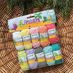 May include: A selection of Amigurumi yarn balls in a range of colours, including white, yellow, pink, orange, red, green, purple, grey, and teal. The yarn is 100% cotton, ideal for crochet projects. The package features the word "AMIGURUMI".