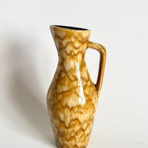 May include: A small, brown ceramic vase with a white glaze and a wavy pattern. The vase has a handle and a narrow opening.