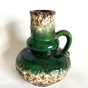 May include: A green and brown ceramic vase with a textured surface and a handle. The vase has a bulbous shape and a narrow neck.