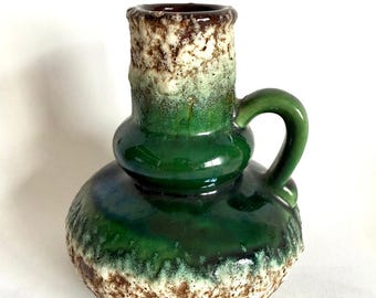 May include: A green and brown ceramic vase with a textured surface and a handle. The vase has a bulbous shape and a narrow neck.