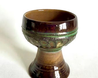 May include: A brown ceramic goblet with a green and gold design. The goblet has a wide bowl and a tall, slender stem.