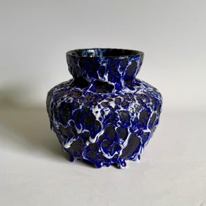 May include: A small, blue and white ceramic vase with a textured, dripping glaze. The vase has a rounded body and a wide opening.