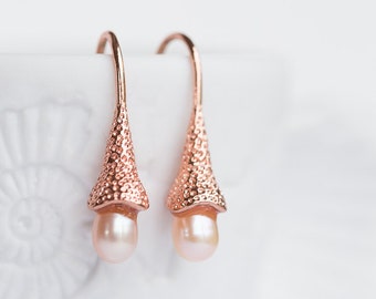 Könnte beinhalten: Ein Paar Ohrringe aus Roségold mit einem strukturierten Design und einem einzelnen Perlenanhänger an jedem Ohrring.