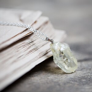 May include: A silver chain necklace with a clear, faceted, yellow crystal pendant. The necklace is lying on a stack of old, cream-coloured paper.