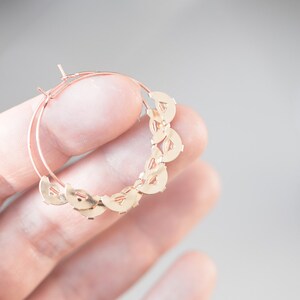May include: Gold hoop earrings with a delicate design of interlocking circles. The earrings are lightweight and have a polished finish.