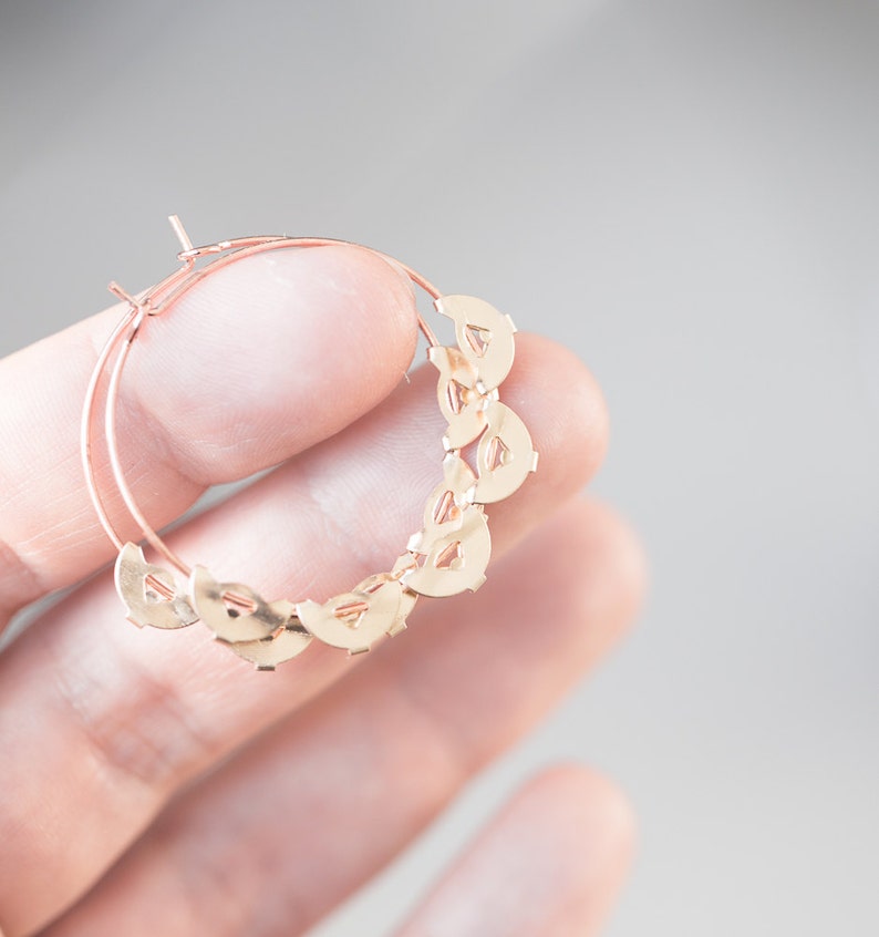 May include: Gold hoop earrings with a delicate design of interlocking circles. The earrings are lightweight and have a polished finish.
