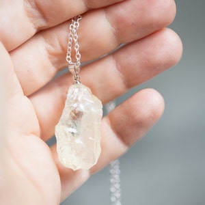 May include: A silver chain necklace with a clear quartz crystal pendant. The crystal is raw and has a natural, irregular shape.