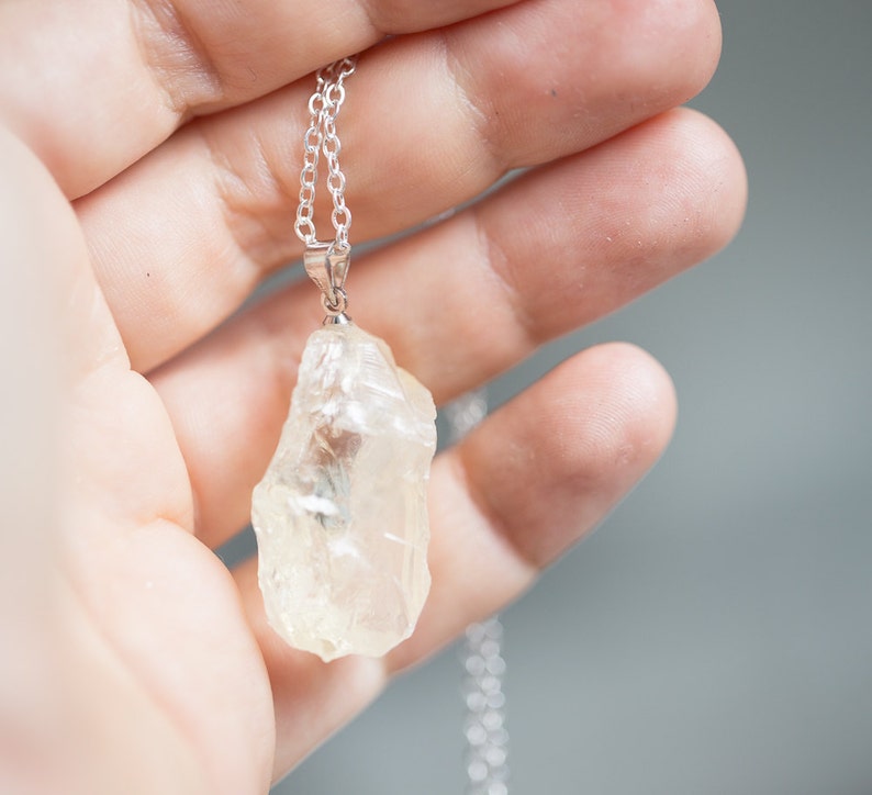 May include: A silver chain necklace with a clear quartz crystal pendant. The crystal is raw and has a natural, irregular shape.