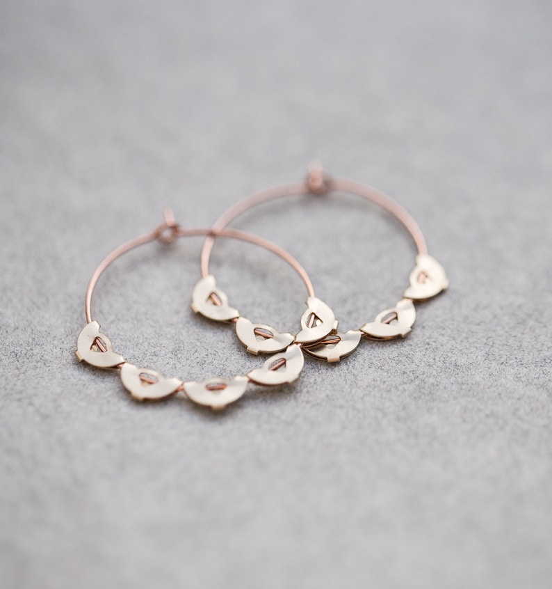 May include: A pair of gold hoop earrings with a decorative design of small, scalloped shapes.