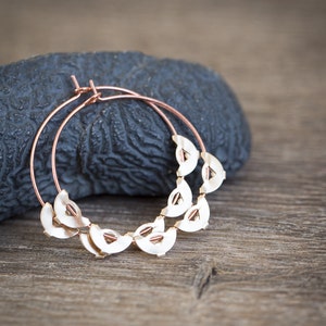 May include: Rose gold hoop earrings with a decorative design of small, half-circle shapes.