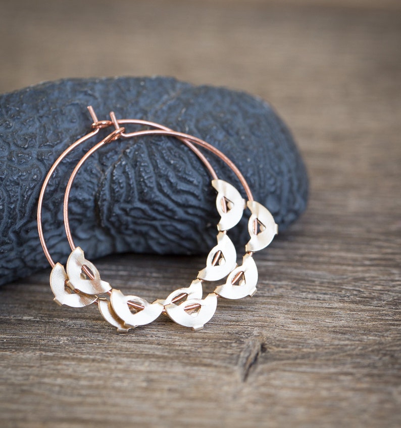 May include: Rose gold hoop earrings with a decorative design of small, half-circle shapes.